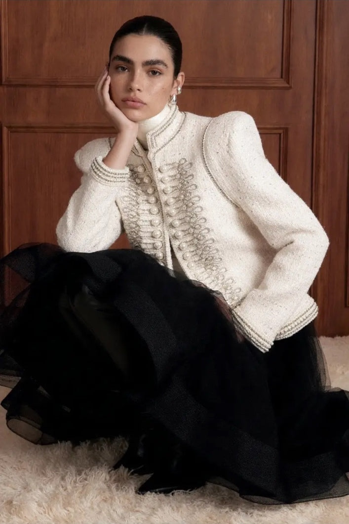 Regent Pearl-Embellished Bouclé Jacket — Ivory jacket seated styling view with stand collar, braided trim and faux-pearl detail