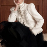 Regent Pearl-Embellished Bouclé Jacket — Ivory jacket seated styling view with stand collar, braided trim and faux-pearl detail