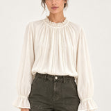 Sabine écru lace-trim blouse, front view showing ruffled collar and fluted cuffs on a model against an ivory background