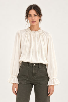 Sabine écru lace-trim blouse, front view showing ruffled collar and fluted cuffs on a model against an ivory background